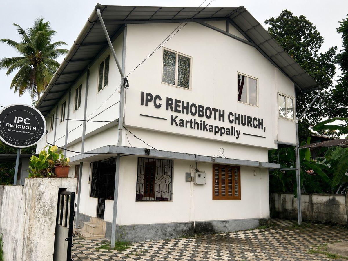 The IPC Rehoboth Church building in Karthikappally — a white two-storey building with the church's name on the wall, beside a coconut palm